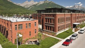 Un bâtiment de style universitaire, composé de plusieurs sections en brique et en verre, entouré d’une pelouse bien entretenue et d’un parking où sont stationnées des voitures.