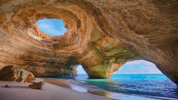 Eine natürliche Felsformation mit einer hohlen Öffnung, einem Sandstrand und Blick auf das Meer.