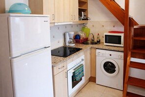 A compact kitchen with a refrigerator, stove, microwave, and washing machine.