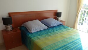 A bedroom with a wooden headboard, two bedside tables with lamps, a bed with a striped bedspread, and a window with curtains. - 238-Apartment with terrace and view on canal (Empuriabrava)