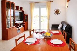 Een eetgedeelte met een houten tafel voor vier personen, een televisie en een bank op de achtergrond.