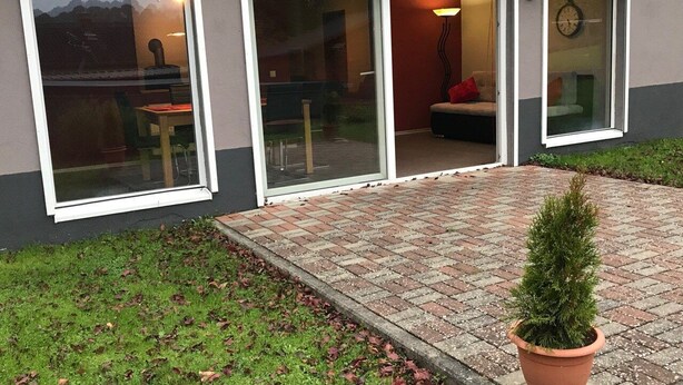 Un bâtiment moderne doté de grandes portes vitrées, d’un chemin en briques et d’une plante en pot.