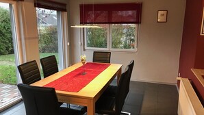 Un coin repas avec une table dressée pour six personnes, un chemin de table rouge et des chaises noires.