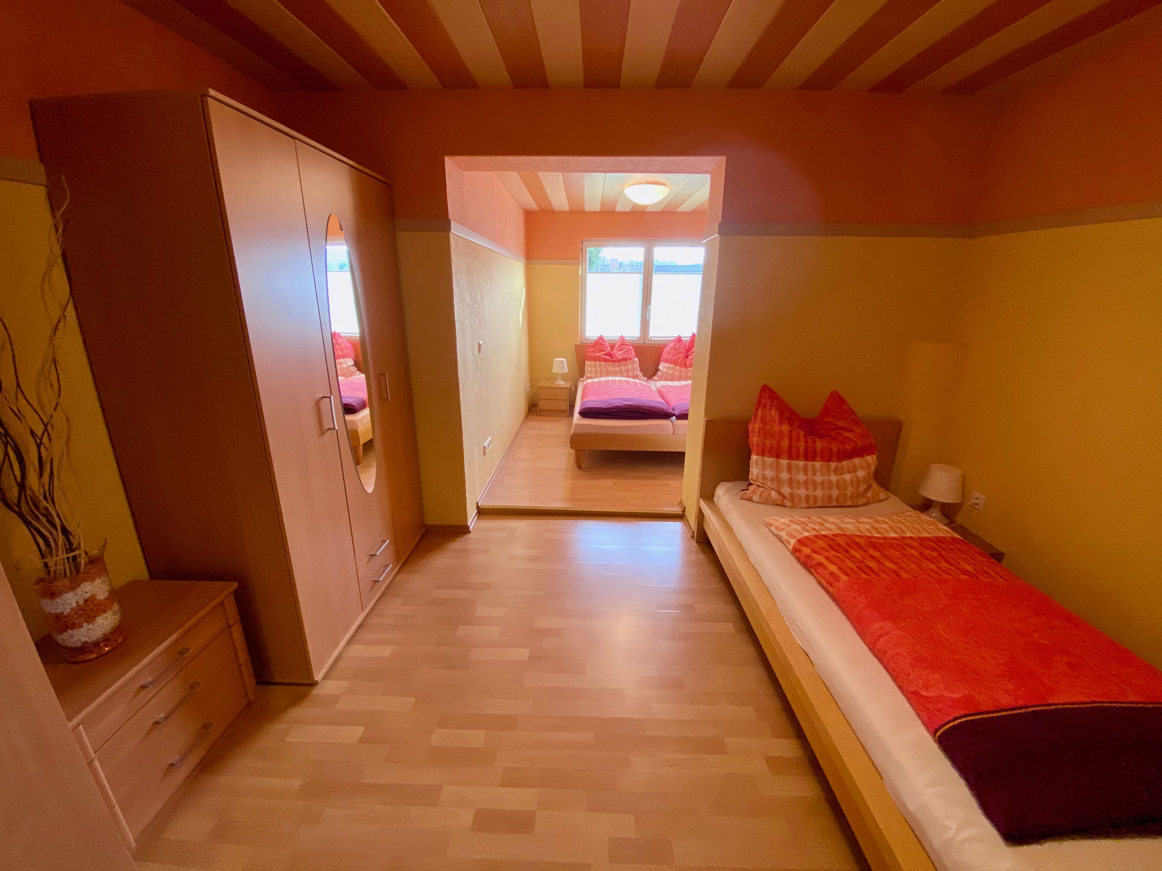 Ein Schlafzimmer mit Bett, Kleiderschrank und kleinem Tisch. Ein Fenster sorgt für natürliches Licht.