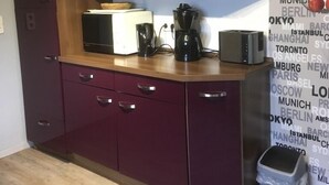 Une cuisine de taille réduite, dotée de meubles de rangement sombres, d’un four à micro-ondes, d’une machine à café et d’une poubelle.