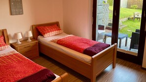 Une chambre avec deux lits simples, une tête de lit en bois, des lampes de chevet et une vue sur un jardin, accessible par une porte vitrée.