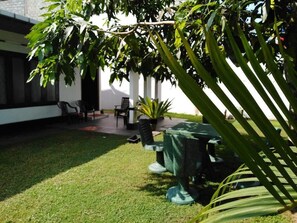 A courtyard with a dining table and chairs, surrounded by greenery and a white building.