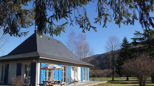A house with a sloped roof, a patio with a table and chairs, and a view of the surrounding landscape.
