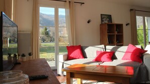 A living room with a sofa, red cushions, a wooden coffee table, a TV, and a bookshelf.