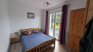 A bedroom with a wooden bed, a nightstand, a lamp, a window with purple curtains, and a view of the outdoors.