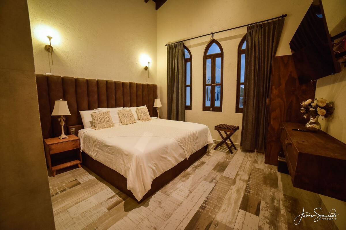 A bedroom with a large bed, two bedside tables with lamps, a wooden bench, and a wooden dresser.