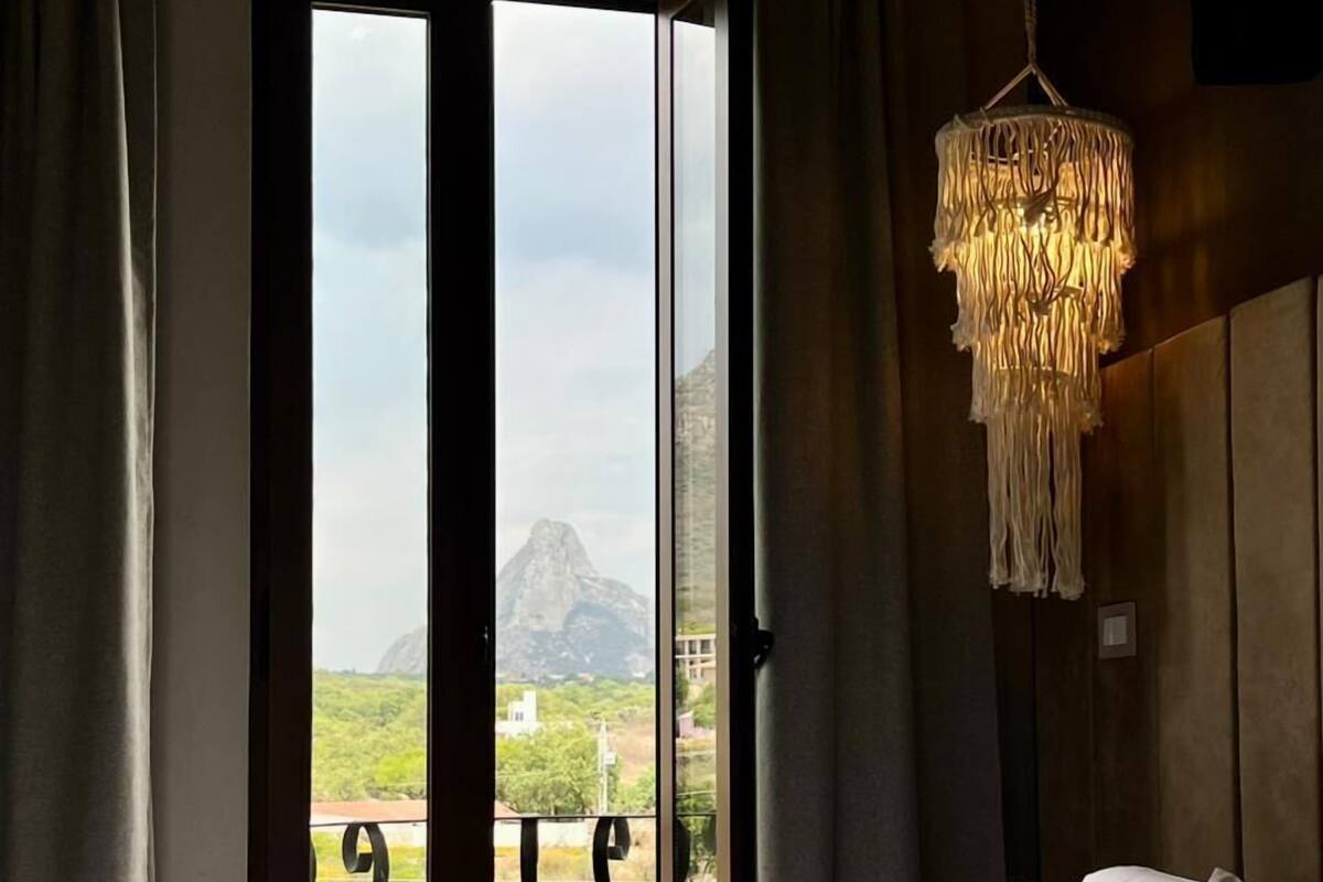 A bedroom with a large bed, a view of a mountain through a sliding door, and a hanging light fixture.