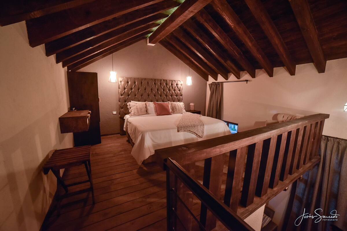 A cozy bedroom with a wooden ceiling, a tufted headboard, and a wooden bench.