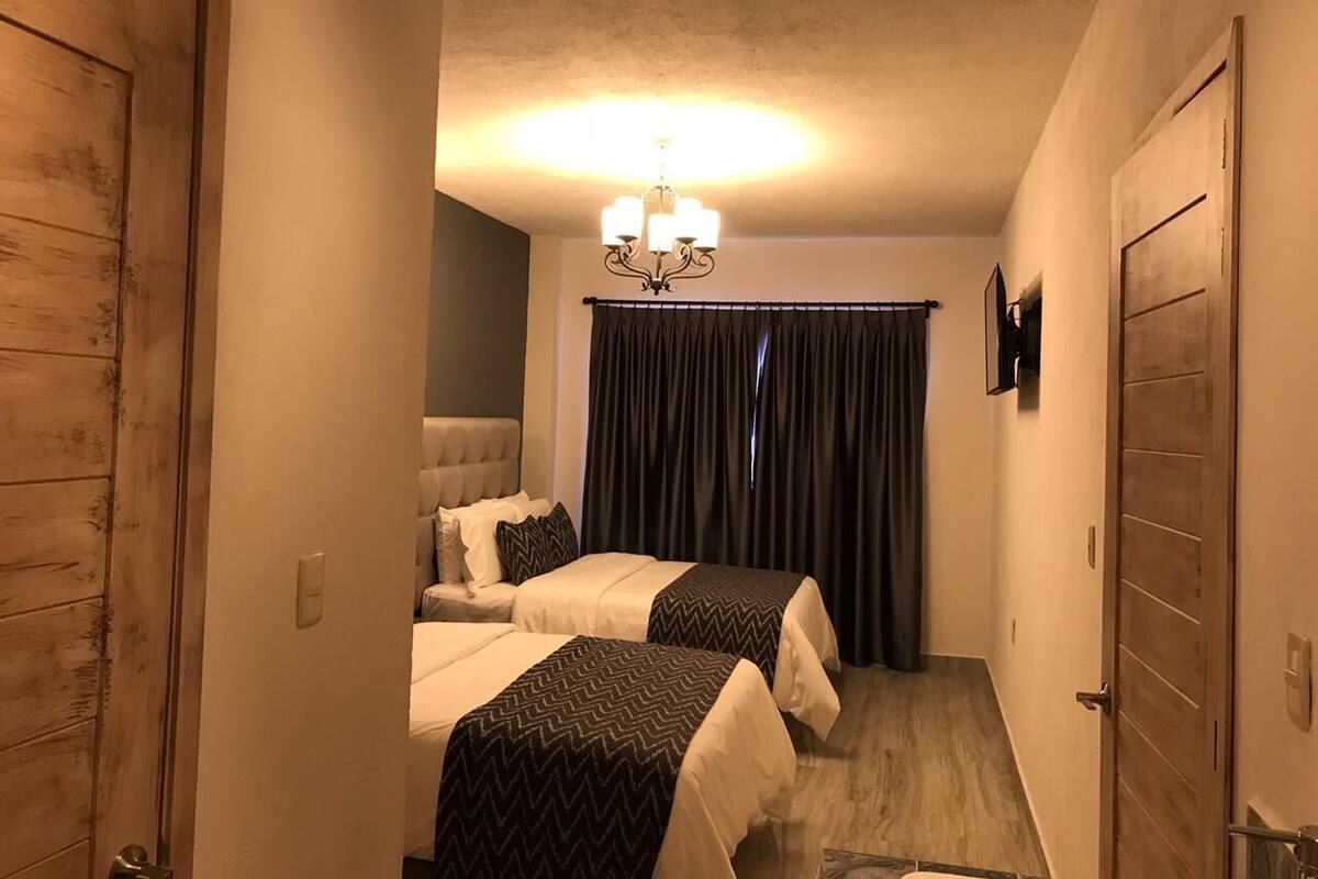 A narrow hallway leading to a bedroom with two beds, a chandelier, and dark curtains.
