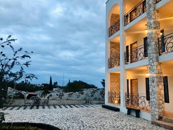 Un edificio de varios pisos con muros de piedra y blanco, balcones con barandillas de hierro forjado y un patio empedrado.