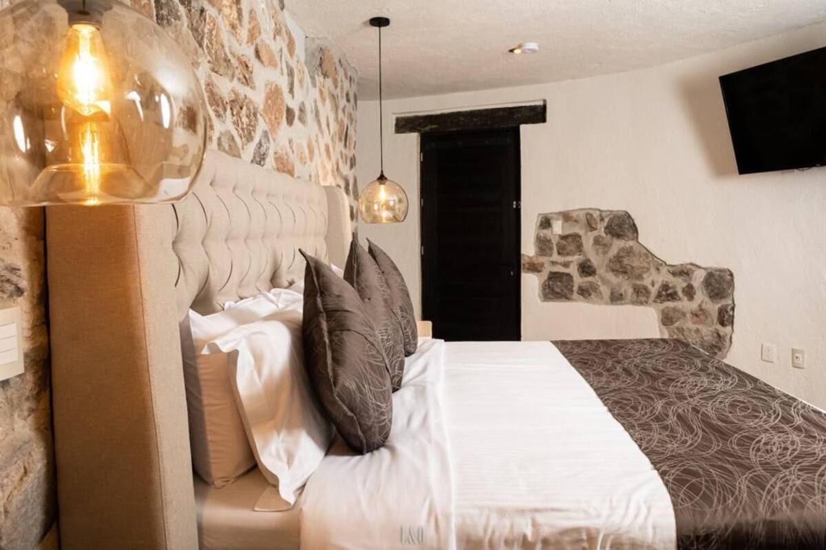 A bedroom with a stone wall, a bed with patterned bedding, a large light fixture, and a mounted TV.
