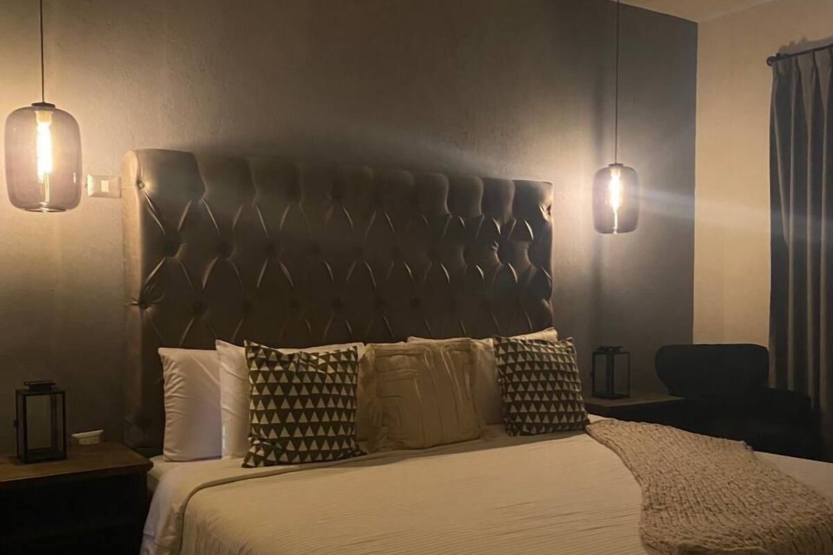 A bedroom with a tufted headboard, a bed with white linens, two bedside tables with lamps, and a chair.