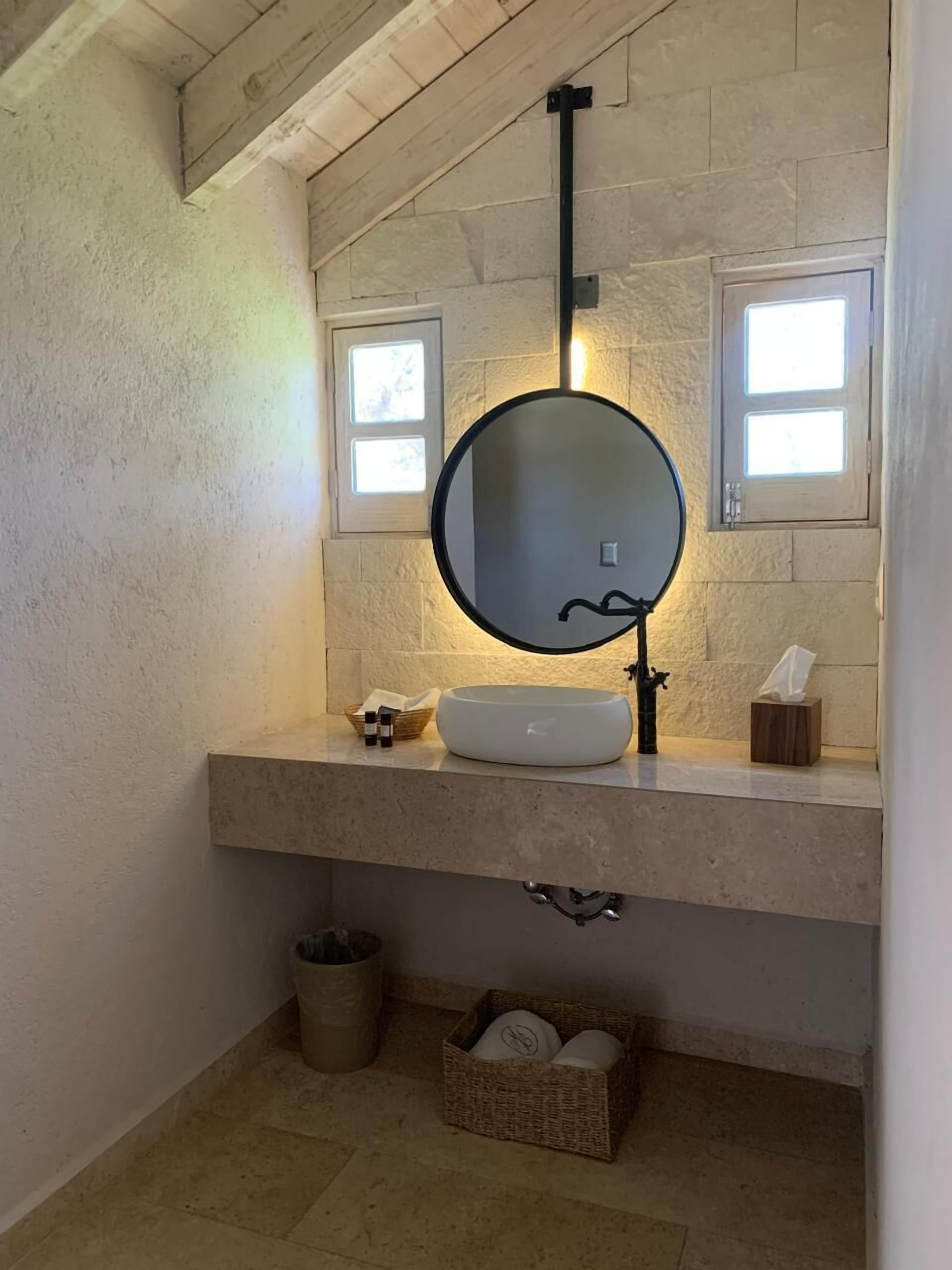A bathroom with a round mirror, a white sink, and a small window above the mirror.