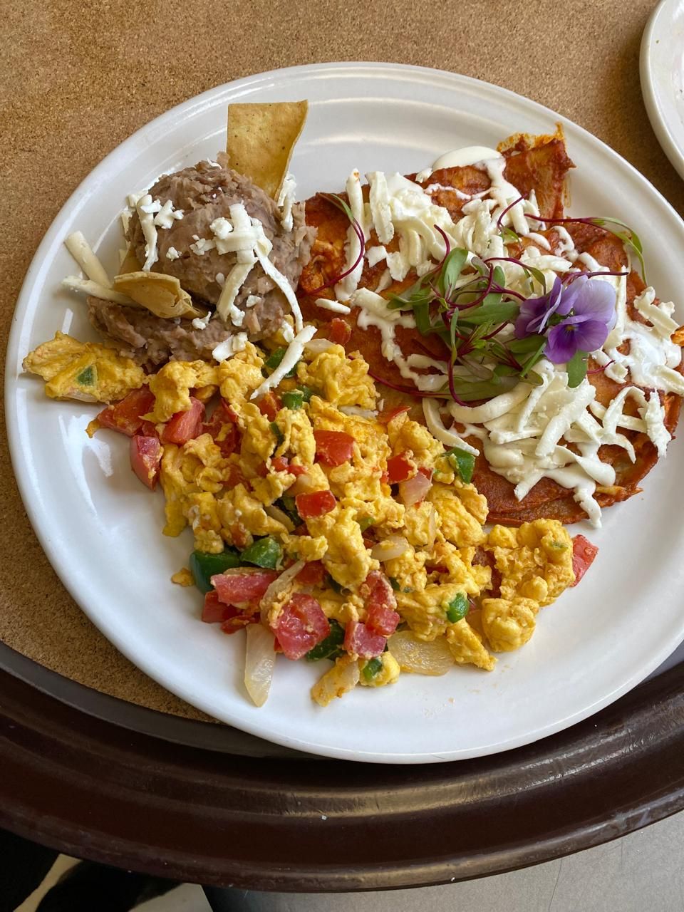 A plate with scrambled eggs, refried beans, and a tortilla topped with cheese and sour cream.