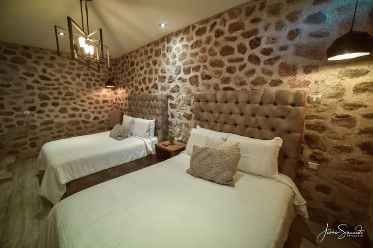 A room with two beds, stone walls, and a chandelier.