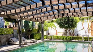 Ein Poolbereich mit Pergola, Liegestühlen und einer Steinmauer.