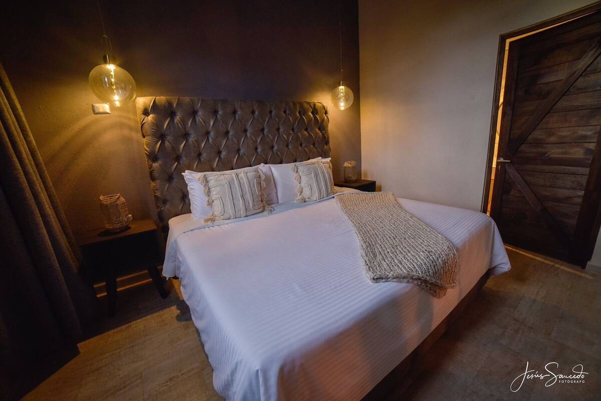 A neatly made bed with a tufted headboard, two bedside tables with lamps, and a wooden door.