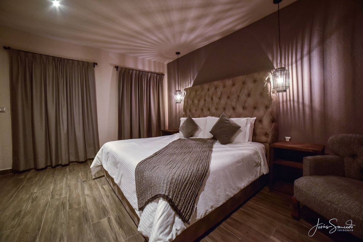 A spacious bedroom with a large bed, a wooden floor, and a nightstand.