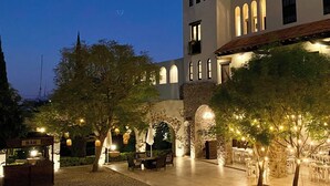 Ein Terrassenbereich im Freien mit Tischen, Stühlen, einer Bar und einem Gebäude mit Rundbogenfenstern und Steinmauern.