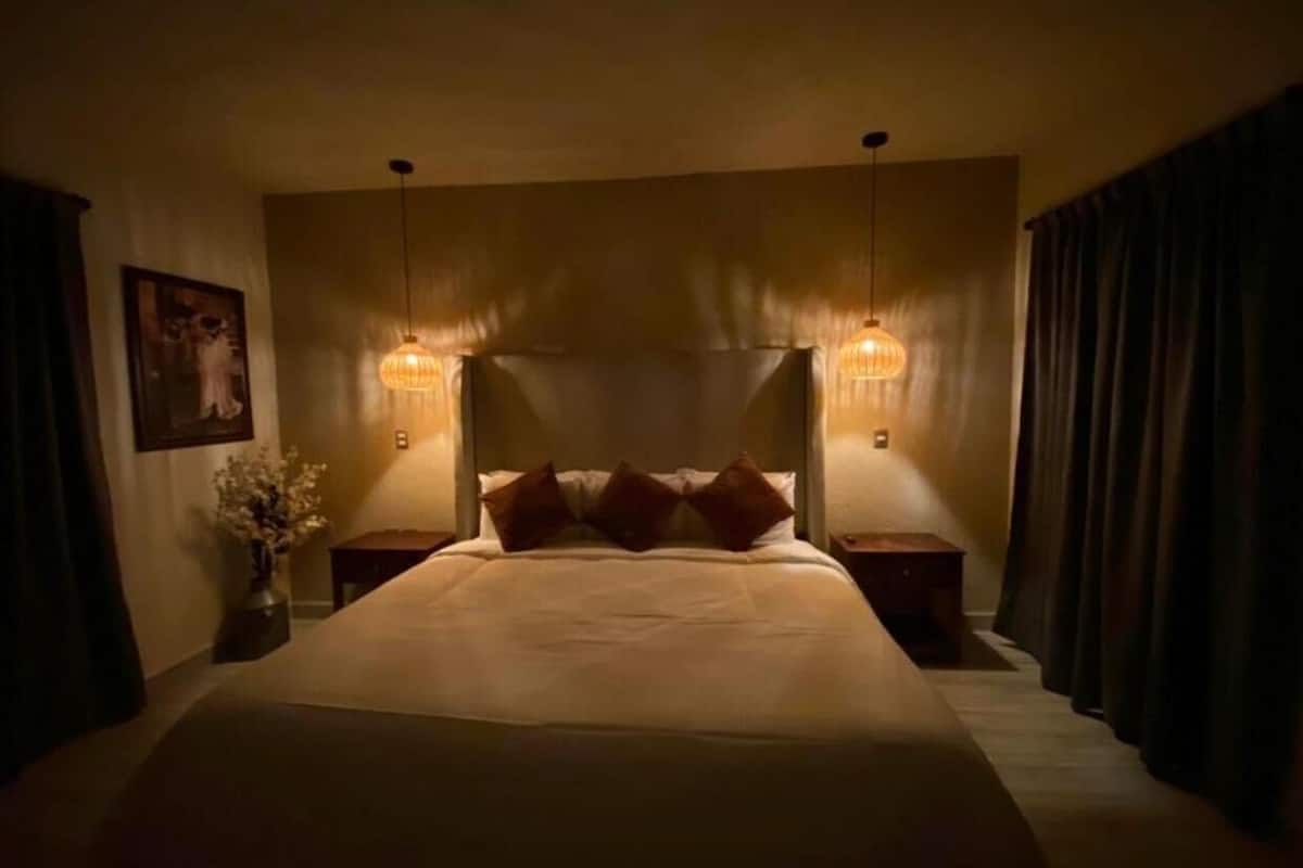 A large bed with a headboard, two bedside tables, and two wall-mounted lamps.