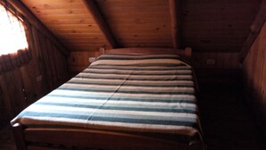 A small, cozy room with a wooden ceiling and walls, a single bed with a striped blanket, and a window on the left side.