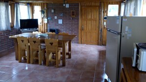 A wooden interior with a dining table and chairs, a television, and a refrigerator.