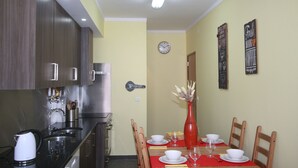 A dining area with a red tablecloth, white plates, and a red vase with flowers. There are wooden chairs and a clock on the wall.