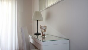 A white bedside table with a glass top, a lamp, and a decorative glass vase.