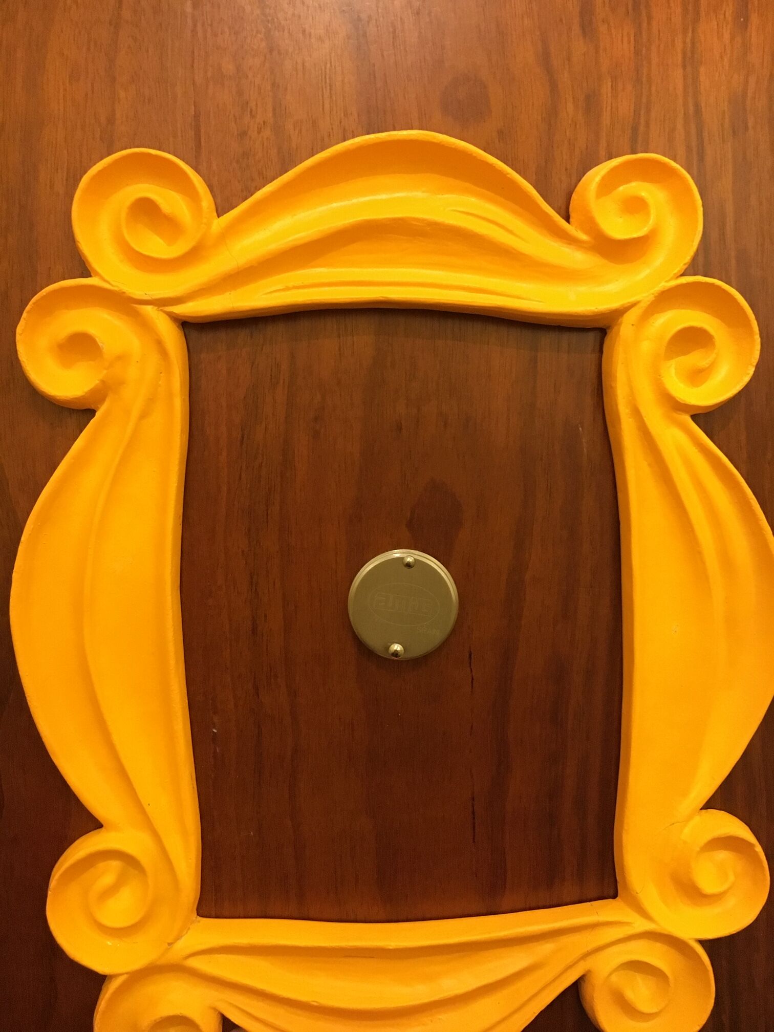 Een houten deur met een gele decoratieve lijst en een ronde messing deurklink.