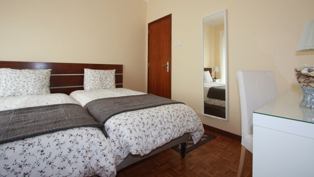 A bedroom with two beds, a wooden headboard, a glass table, and a mirror on the wall.