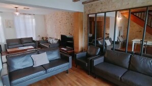 Moderni olohuone, jossa on nahkasohvat, litteänäyttöinen televisio ja suuri peili, joka heijastaa huoneen sisustusta.