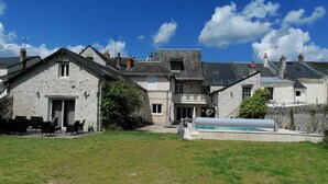 Suuri kivirakennus, jossa on uima-allas, katettu terassi ja nurmikkoalue.