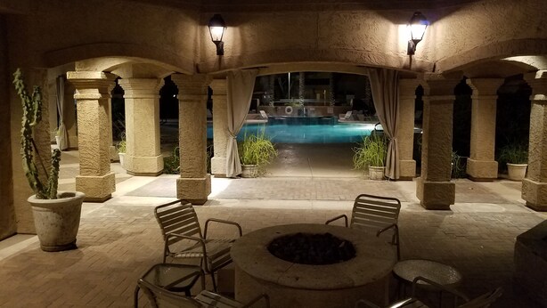 Un patio al aire libre con columnas de piedra, una fogata y una piscina al fondo.