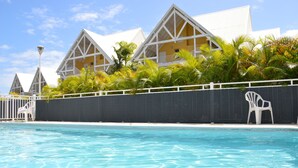 A swimming pool with a white fence and chairs, surrounded by buildings with a triangular roof design. - Caribbean Village, holiday apartment, Guadeloupe, 97180 (Sainte-Anne)
