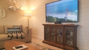 Un salon doté d’un téléviseur à écran plat fixé au mur, d’un canapé agrémenté de coussins à motifs, d’une table basse en bois et d’un meuble avec des portes en verre.