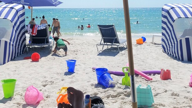 Une scène de plage avec des parasols, des chaises de plage et des personnes dans l’eau.
