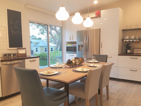 A modern kitchen with a dining table set for two, a refrigerator, and a coffee machine.