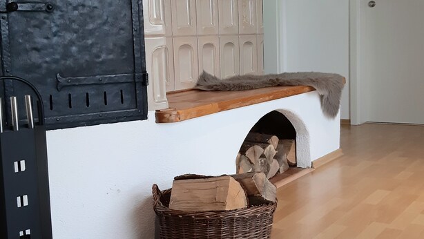 A fireplace with a white mantel, a basket of firewood, and a door in the background.