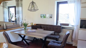 A modern kitchen with a wooden table, two chairs, a bench, and a hanging light fixture.