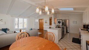 Una cocina moderna con armarios blancos, una isla central y un comedor con mesa y sillas de madera.