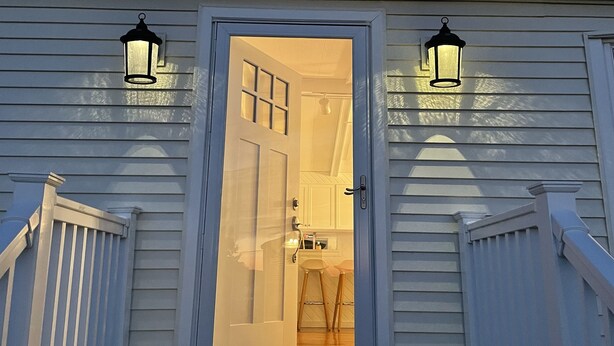 Una casa blanca con puerta principal, dos faroles exteriores y una escalera de madera.