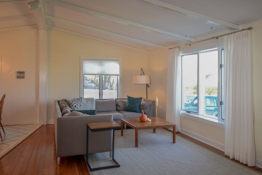 Ein modernes Wohnzimmer mit einer Couch, einem Couchtisch und einer Lampe. Ein Fenster mit Vorhängen bietet einen Ausblick ins Freie.