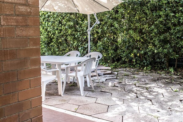 A patio area with a table and chairs, a brick wall, and a hedge in the background.