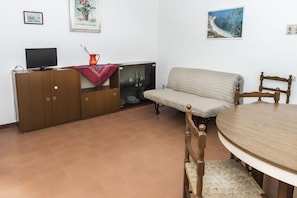 A room with a TV, wooden cabinet, sofa, and a round table.
