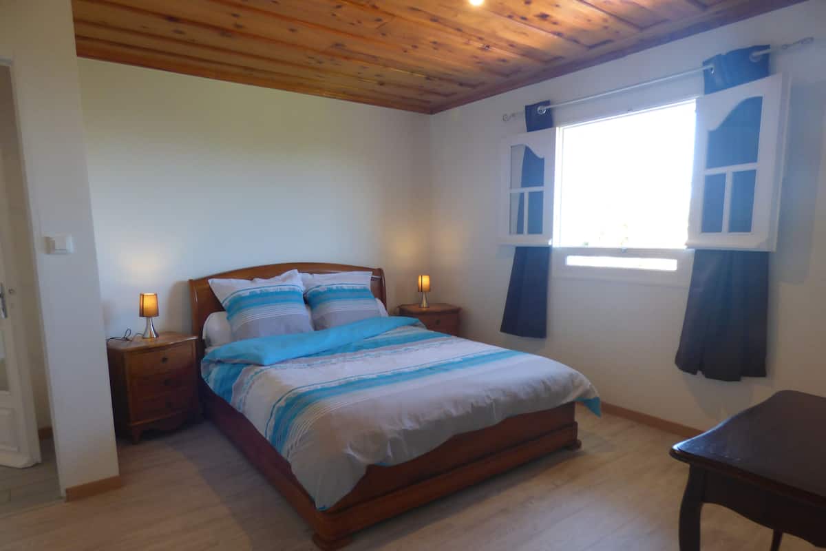 Un dormitorio con cama de madera, mesitas de noche, una ventana con cortinas y suelo de madera.